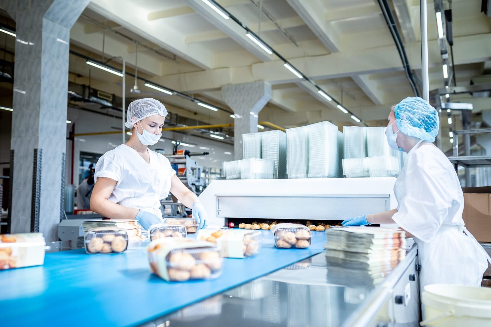 Two operators in hairnets and gloves packing product at the end of a bakery line